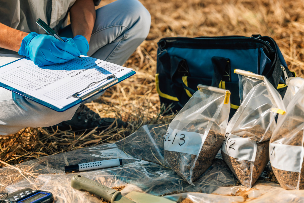 A scientist writing down findings on a clipboard while looking over plastic baggies filled with collected soil samples.